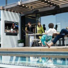 Four people watching basketball on Samsung’s The Terrace outdoor TV by the pool.