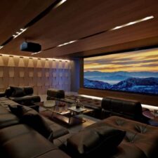 A home theater with sectionals, a projector, a large screen, and acoustic paneling.