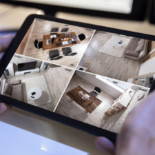 A shot of a person holding a tablet showing different monitored rooms within their home for home security purposes.