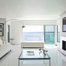 A living room with a view of the ocean. In the room are an inset flat-screen TV and Sonance invisible speakers.