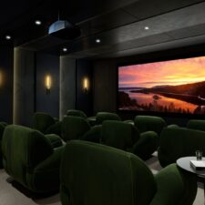 A home theater with plush green seating, a large projector screen, and a Sony projector.
