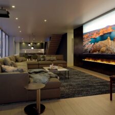 Media room with a projector and large screen. A lit fire feature extends the length of the screen.